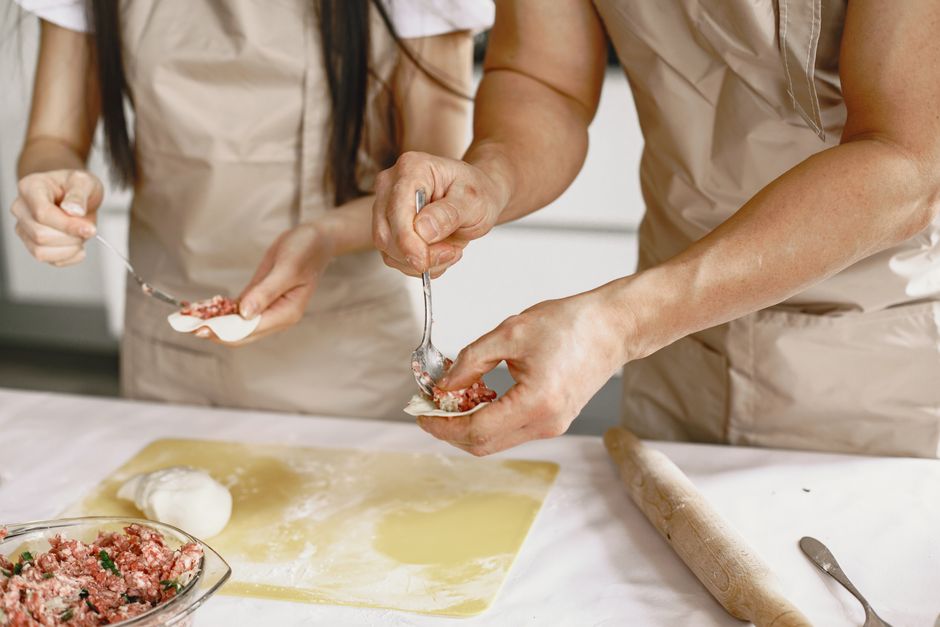 Two people preparing homemade dumplings with minced meat filling in a kitchen setting.