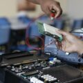 Close-up of hands working with electronics equipment and circuit board in a lab setting.